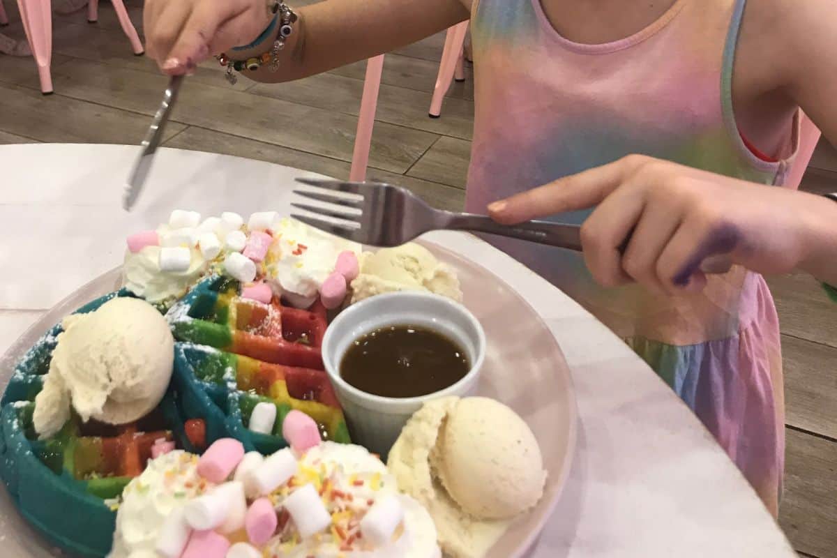 Child eating a rainbow waffle at Kawaii Cafe